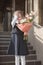 A primary school student in a blue uniform stands outdoors and holds a bouquet of flowers