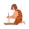 Primitive archaic man or caveman dressed in skin clothes lighting fire through friction by grinding piece of wood or