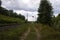 Primitive road along the railway turning to the left among the forest landscape, summer cloudy view.