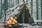 Primitive survival shelter in winter forest with Christmas garland near campfire