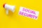 Printed words social security near megaphone on yellow background with computer keyboard top view space for text