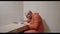 Prisoner in an orange jumpsuit writes a letter at a table in a prison cell.