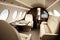 Private jet interior features plush leather seats, spacious cabin, large windows, high-end finishes, and a table.