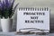 PROACTIVE NOT REACTIVE - words in a notebook on a light background with glasses and a bouquet of lavender