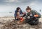 Problems of environmental pollution and oceans, a young couple in orange gloves cleans plastic and garbage in a black trash bag on