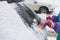 Process of cleaning a car from snow in the morning, girl removing snow from windscreen with a window scraper brush after snowstorm