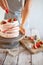 Process of decorating meringue cake with whipped cream and fresh strawberry