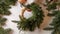 The process of making a Christmas wreath. Top view of florist hands fix the twine of the fir branches to the straw base.