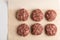 The process of making meatballs from beef meat. Six unroasted raw meat balls laid out on baking paper. View from above.