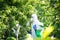 The process of treating plants with pesticides. Farmer in protective suit and mask walking trough orchard with pollinator machine