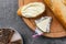 Processed triangle cheese in foil and baguette on wooden board on gray background.