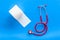 Proctology concept with toilet paper roll and stethoscope on blue background top view