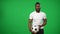 Professional African American footballer juggling ball on green screen and looking at camera. Portrait of serious