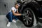 Professional African male worker in overalls and black protective gloves, cleaning alloy wheels rims of luxury car with