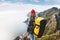 Professional alone expeditor wearing backpack and red hat standing on the edge cliff mountain. Extreme tourist on high rock above