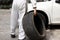 Professional automotive mechanic in uniform holding tire for fixing car at the garage background. Auto repair service.