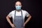 Professional bald butcher or fishmonger in white t-shirt and black and white apron on dark background. Man wearing blue face mask