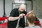 Professional barber cuts the client with scissors and a comb with a serious face. Male hairdresser creates stylish haircut for
