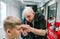 Professional barber is focused on trimming a young client`s hair. Professional hairdresser does a hairstyle for a young man in a