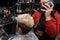 A professional barber holds a hair dryer in his hands and dries the hair of a young client guy in the salon before a haircut