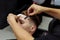 Professional barber with open cutthroat razor shaves hair on man`s temples. Attractive male is getting a modern haircut