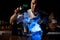 Professional bartender pouring a brown alcoholic drink from the steel shaker to the glass under blue light