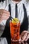 A professional bartender puts a slice of lemon in a red chilled alcoholic cocktail with bar tweezers in glass at a nightclub