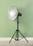 Professional beauty dish reflector on tripod near pale green wall in room. Photography equipment