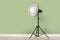 Professional beauty dish reflector on tripod near pale green wall in room, space for text. Photography equipment