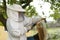 professional beekeeper in protective workwear inspecting honeycomb frame at apiary. beekeeper harvesting honey