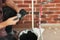Professional builder filling fugue with grout gun near brick wall, closeup. Tiles installation process