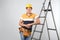 Professional builder near metal ladder on grey background