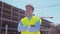 Professional builder standing in front of construction site. Foreman in hardhat helmet and vest. Office building and