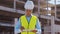 Professional builder standing in front of construction site. Foreman in hardhat helmet and vest. Office building and