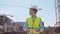 Professional builder standing in front of construction site. Foreman in hardhat helmet and vest. Office building and