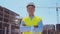 Professional builder standing in front of construction site. Foreman in hardhat helmet and vest. Office building and