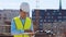 Professional builder standing in front of construction site. Foreman in hardhat helmet and vest. Office building and
