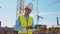 Professional builder standing in front of construction site. Foreman in hardhat helmet and vest. Office building and