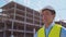 Professional builder standing in front of construction site. Foreman in hardhat helmet and vest. Office building and