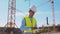 Professional builder standing in front of construction site. Foreman in hardhat helmet and vest. Office building and