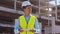 Professional builder standing in front of construction site. Foreman in hardhat helmet and vest. Office building and