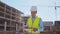 Professional builder standing in front of construction site. Foreman in hardhat helmet and vest. Office building and