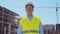 Professional builder standing in front of construction site. Foreman in hardhat helmet and vest. Office building and