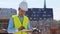 Professional builder standing in front of construction site. Foreman in hardhat helmet and vest. Office building and