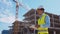 Professional builder standing in front of construction site. Foreman in hardhat helmet and vest. Office building and