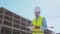 Professional builder standing with tablet computer in front of construction site. Foreman in helmet and vest. Office