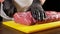 A professional butcher in black gloves slices a piece of raw meat for steak from entrecote with a sharp knife. The cook