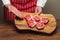 Professional butcher in classic red and white apron holding cutting board with fresh uncooked lamb loin chops. Meat industry