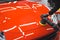 Professional car detailing expert using machine polish on a bonnet of a vivid red sports car. Specialistic equipment for