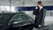 Professional car salesman is telling interested buyer about luxurious car in motor show while man istalkinng with dealer